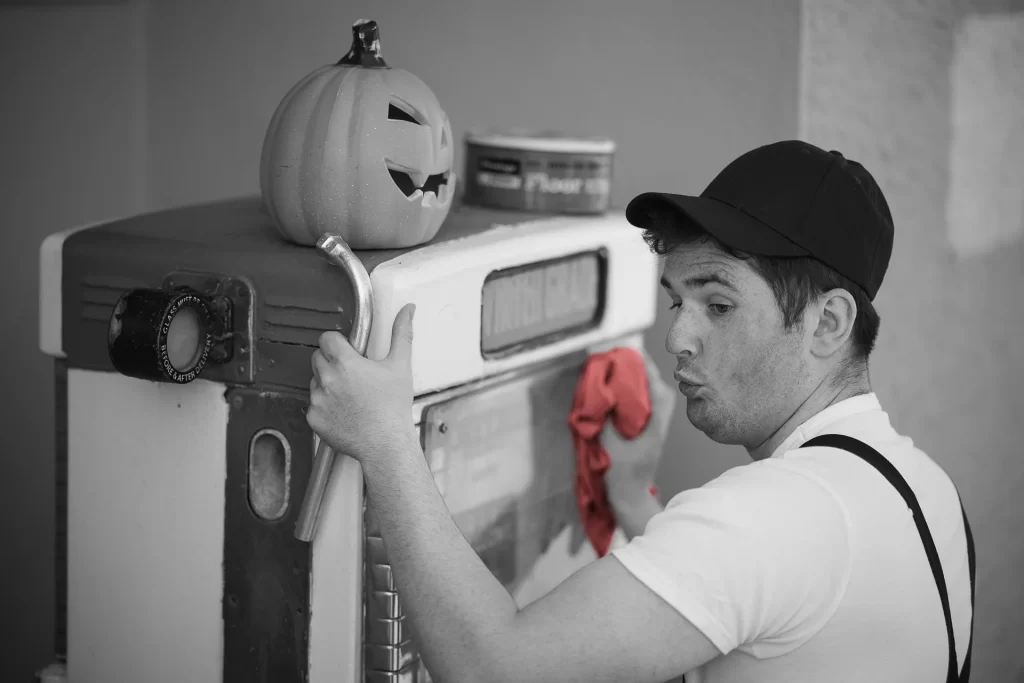 Until Stills Photography from retro 1960s sci-fi horror movie pastiche "Mad Cows from Planet Moo." Benny wolf whistles at Sharon as she bends down to place a Halloween decoration.