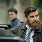 Unit still from Irish feature film Perdu, actor Brian Matthews Murphy in character as detective Reilly, gazes pensively around outside his car, his young partner blurred in the background.